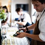 Waitstaff pouring champagne into glasses at a sophisticated indoor event.